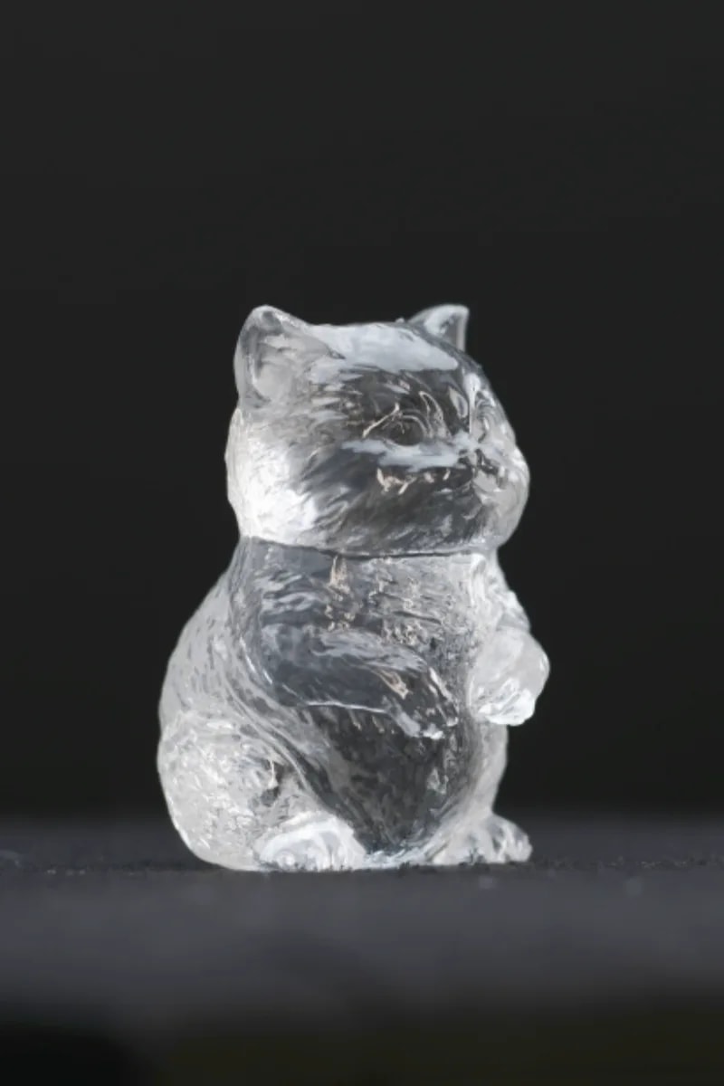 Front view of a small clear quartz cat sitting upright, ears raised, with incised fur lines across the face and chest.
