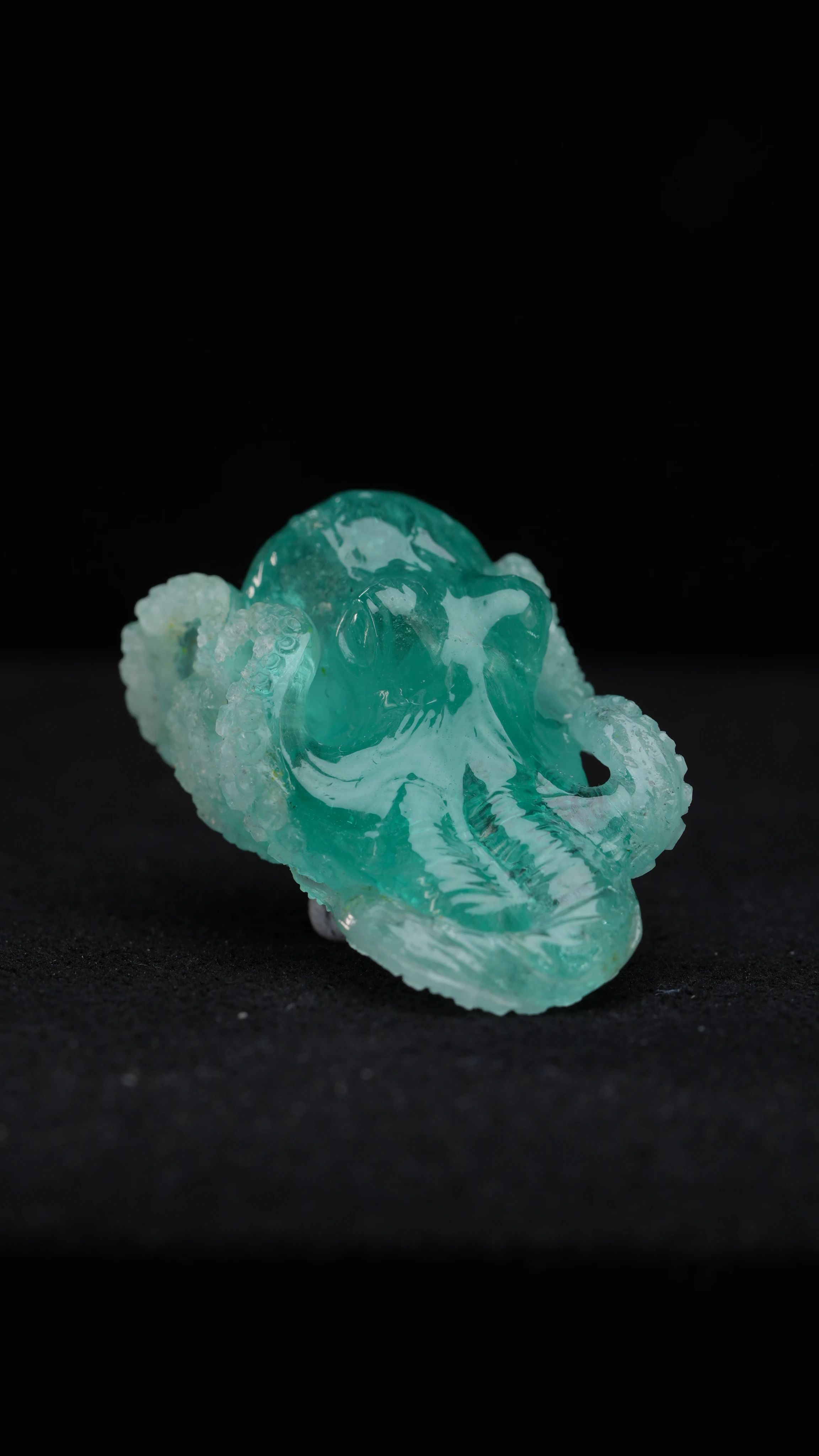 The Emerald Octopus, a hand carved emerald octopus with its mantle raised and two arms curled into spirals